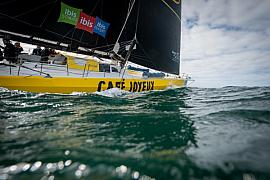 Coque jaune du voilier IMOCA Café Joyeux fendant les vagues à fleur d’eau lors d’une course au large.