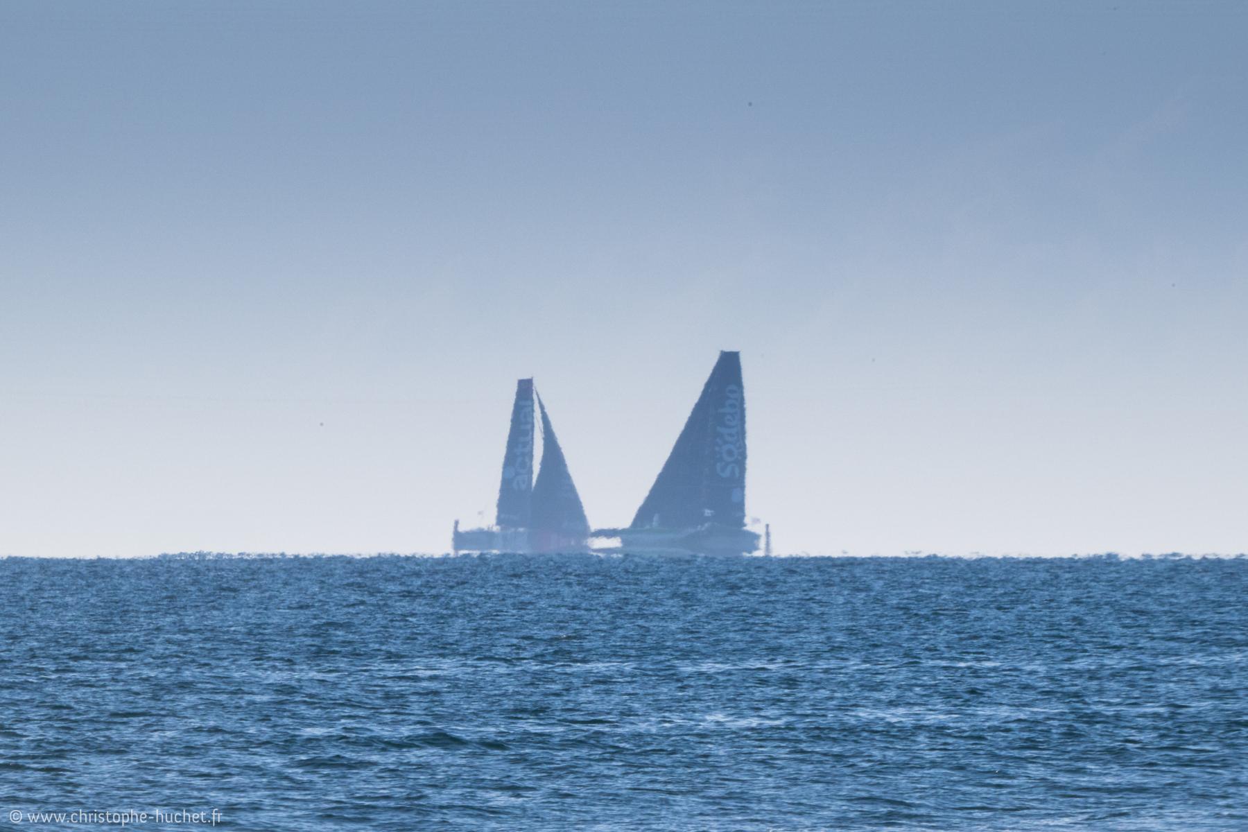 Deux trimarans Ultim (Actual et Sodebo) naviguant sur la ligne d’horizon par temps clair au large de Lorient lors d’une course.