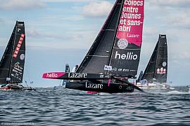 Trimaran Lazare noir et rose naviguant à grande vitesse sur l’eau à Lorient parmi d’autres voiliers de course.
