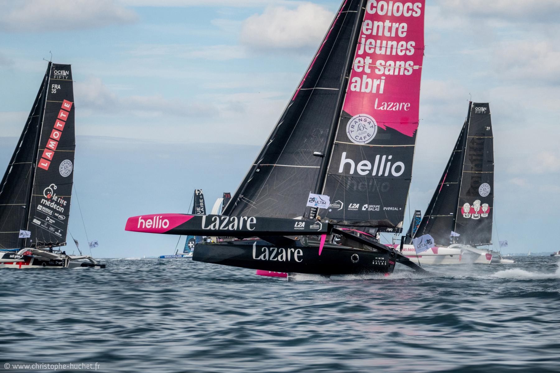 Trimaran Lazare noir et rose naviguant à grande vitesse sur l’eau à Lorient parmi d’autres voiliers de course.