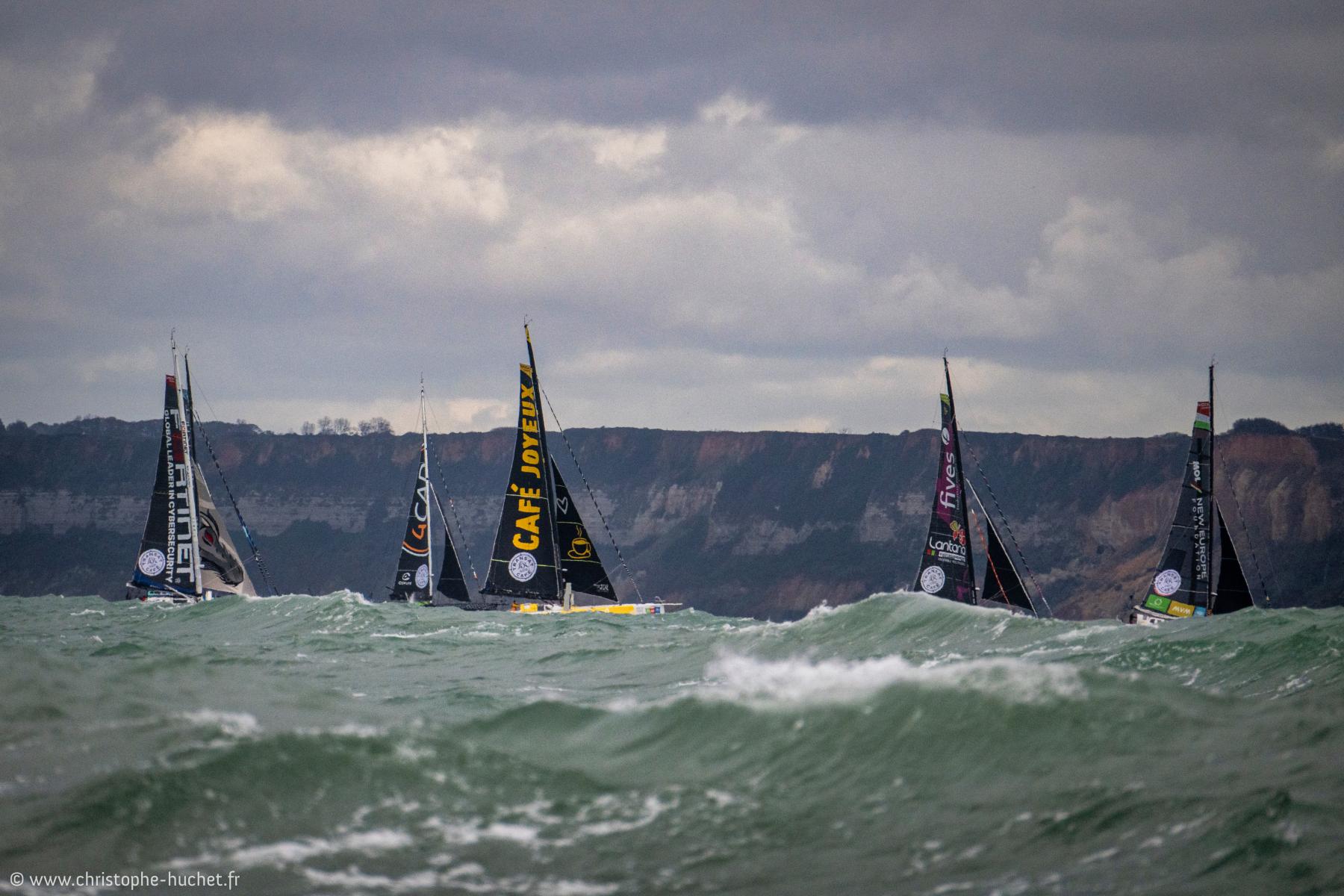 Voiliers IMOCA dont Café Joyeux sur mer agitée devant les falaises du Havre par temps couvert.