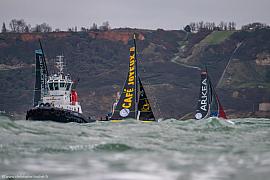 Remorqueur et voiliers Imoca Café Joyeux et Arkea en mer agitée devant les falaises du Havre sous un ciel gris.