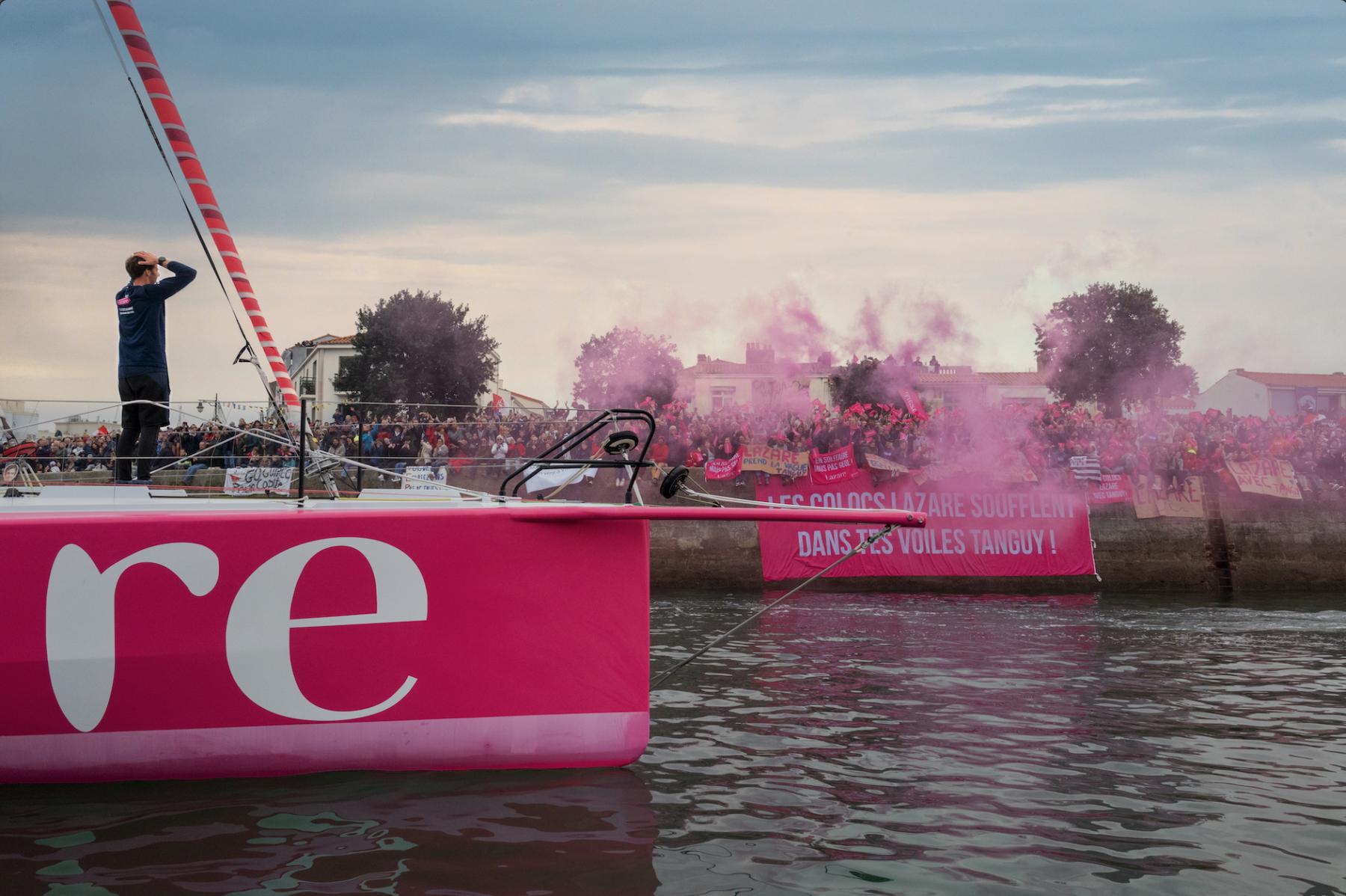 Coque rose,l’ IMOCA Lazare et skipper Tanguy Le Turquais dans une fumée rose lors du départ aux Sables d’Olonne.
