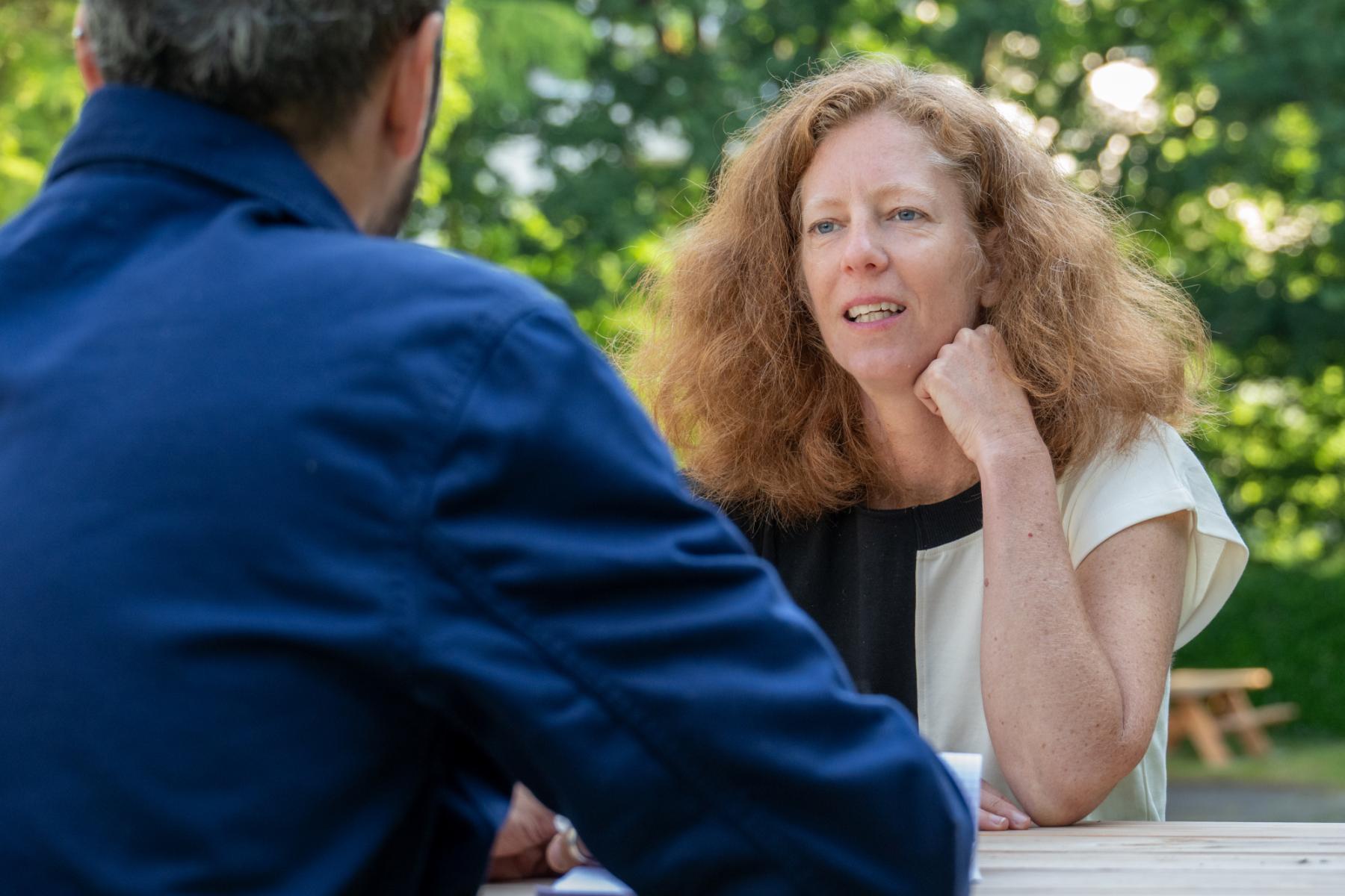 Femme rousse en discussion lors d’une formation en plein air, lumière du jour sur fond de parc verdoyant.