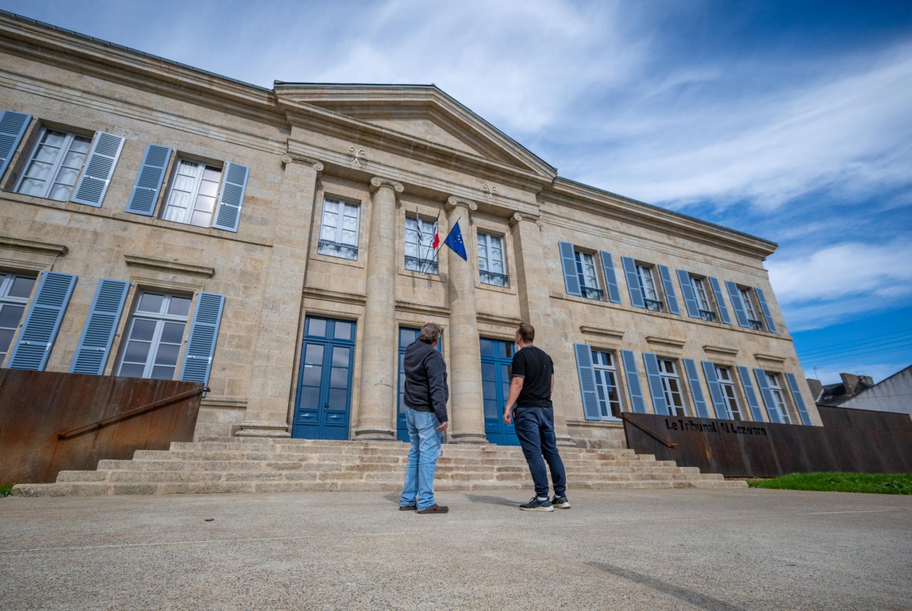 Deux hommes face au bâtiment néoclassique du Tribunal de Pontivy, façade en pierre claire et menuiseries bleues.