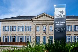 Façade en pierre du tribunal de Pontivy avec volets bleus et totem Région Bretagne sous un ciel clair ensoleillé.