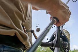 Hameçon avec appât et canne à pêche tenue par un homme en extérieur, mise au point précise sur le matériel.