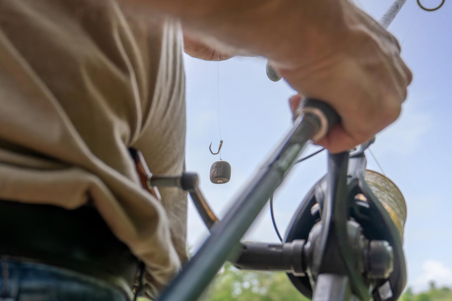 Hameçon avec appât et canne à pêche tenue par un homme en extérieur, mise au point précise sur le matériel.