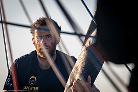 Marin barbu concentré derrière les cordages d’un voilier de course lors d’une arrivée en mer sous un soleil rasant