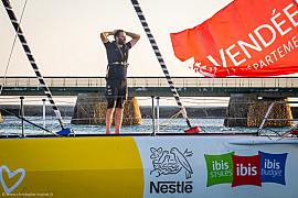 Skipper sur voilier jaune et blanc avec drapeau rouge au coucher du soleil devant la digue des Sables-d’Olonne