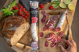 Saucisson fuet tranché sur planche en bois avec pain de campagne, tomates cerises et main sous une lumière chaude