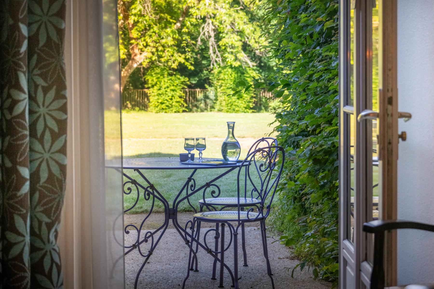 Mobilier en fer forgé sur une terrasse ensoleillée ouvrant sur un parc arboré au Château de Keravéon.