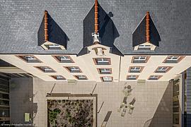 Vue verticale drone sur un toit en ardoise, facade beige et cour pavée ensoleillée avec mobilier vert.