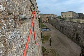 Vue immersive d’escalade avec une corde orange et mousqueton sur muraille avec des militaires