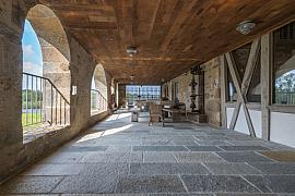 Terrasse abritée sous des arcades en pierre avec plafond en bois massif, sol en dalles de granit et mobilier rustique.