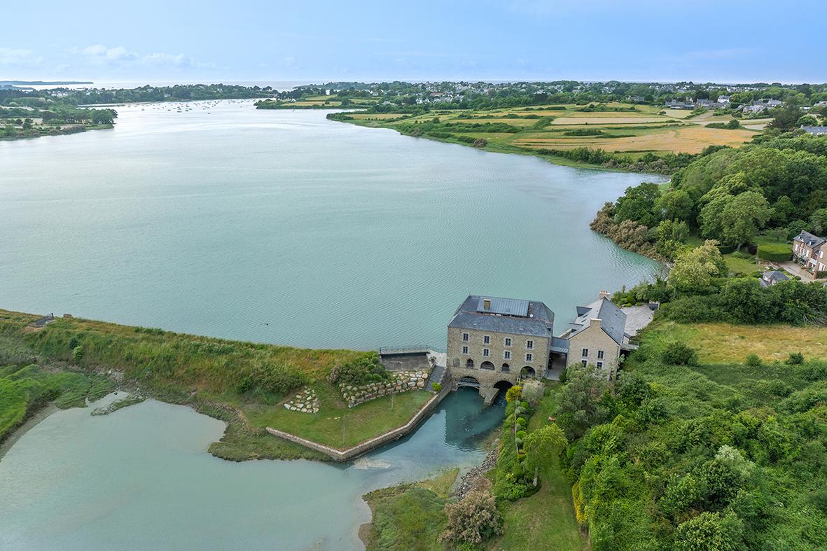 Moulin à marée de pierre entouré de végétation et d’eau, vue aérienne drone sous lumière naturelle.
