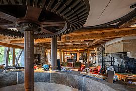 Ancien mécanisme de moulin intégré dans un salon contemporain avec poutres en bois et murs de pierre traditionnels.