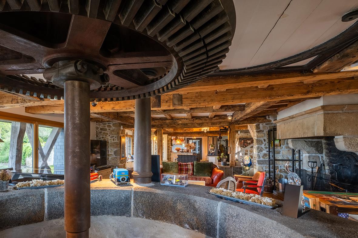 Ancien mécanisme de moulin intégré dans un salon contemporain avec poutres en bois et murs de pierre traditionnels.